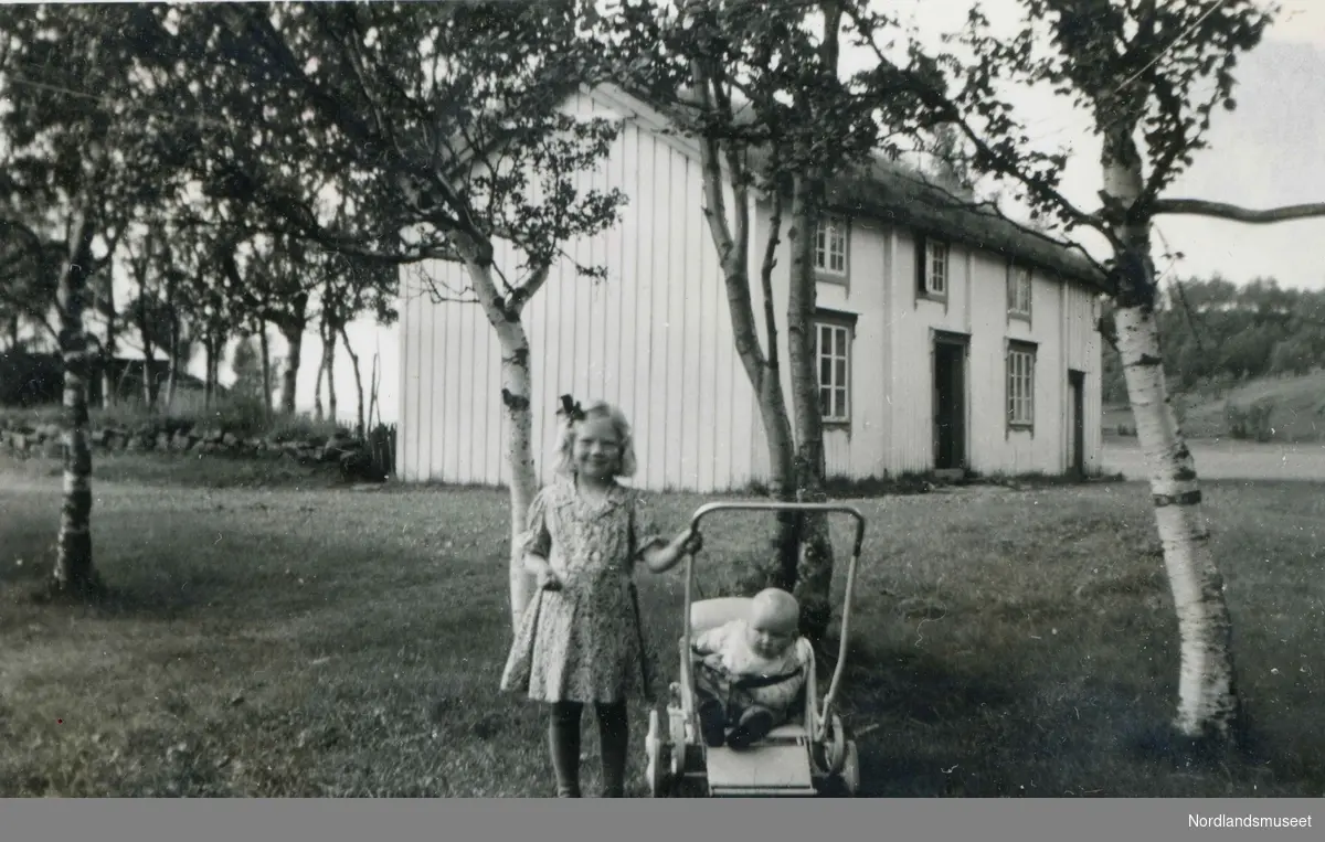 Mary Korsaksel (f. 1938) er ute og triller sin lillesøster Karin Marie (f. 1942) i sportsvogn på Korsaksel på Engeløya.