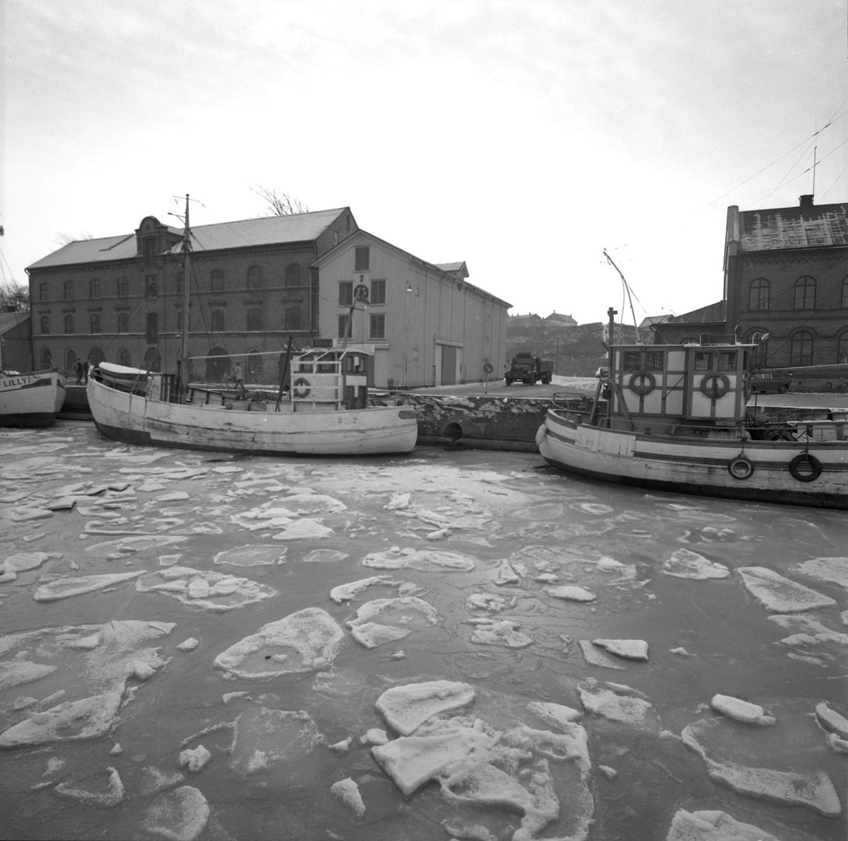 Tidningsartikel med rubriken "Fyra nyårsbåtar i Varbergs hamn" publicerad i Hallands Nyheter 1970-01-02. Till vänster ses hamnmagasinet från 1874 med Lundqvists trämagasin och till höger tullhuset.
(Bilderna inlagda i omvänd ordning mot id-numren)