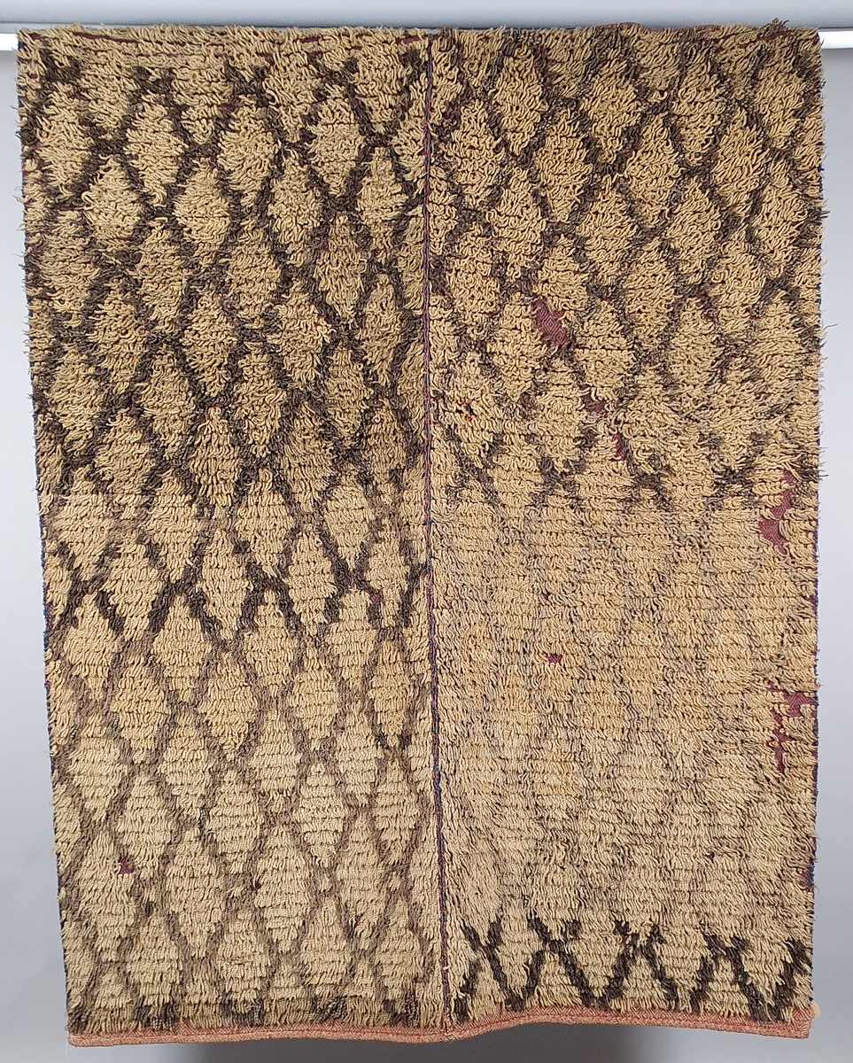 Knytteteppe, sydd sammen av to deler. På forsiden er det knyttet floss med diagonale store ruter i beige og brunt. Baksiden har små, tette diagonale romber i burgunder-farger.