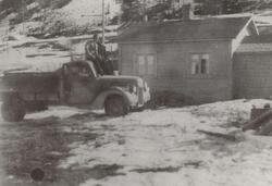 2 menn sitter på en lastebil ved et lite hus/brakke (gjenrei