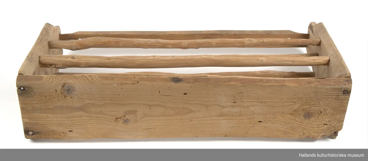Hylla av omålat trä. Självstående konstruktion i rektangulär utformning. Dekorerad med facetterade ytor. Hyllan är ihopfasad med hjälp av grov sprik och sinkning. Hyllans ram är konstruerad av en övre bräda av furu med bottenbräda av gran och sidor av ädelträ. Hyllan har två våningsplan med ribbor av klyvt envirke. 

Den övre brädan har två hål (17 mm diameter) vid respektive kortsida, vilket troligtvis är spår efter en bärkonstruktion eller upphängning.