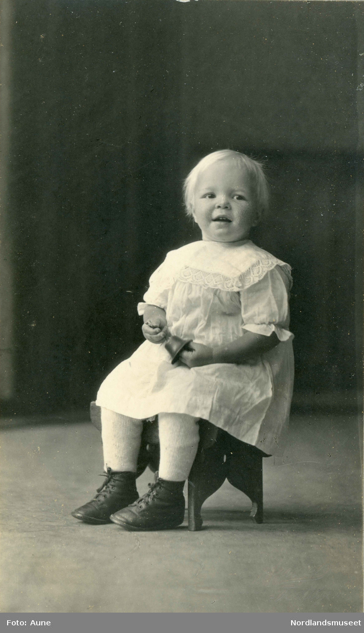 Portrett av en liten jente som sitter på en stol.