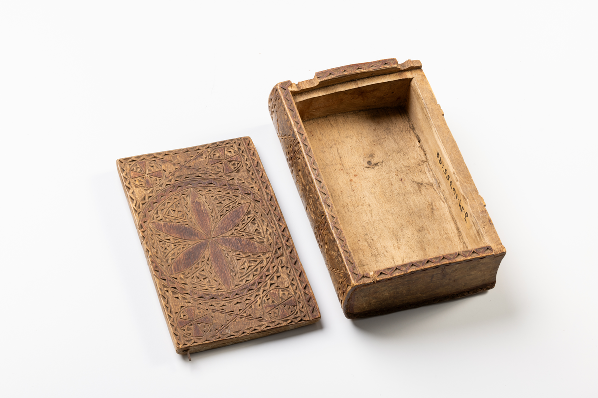 Skrin (ask) av trä i form av en bok. Rikt dekorerad i karvsnitt, med spår av röd färg. På ryggen snidade initialer och årtal: "MSD", "1820".