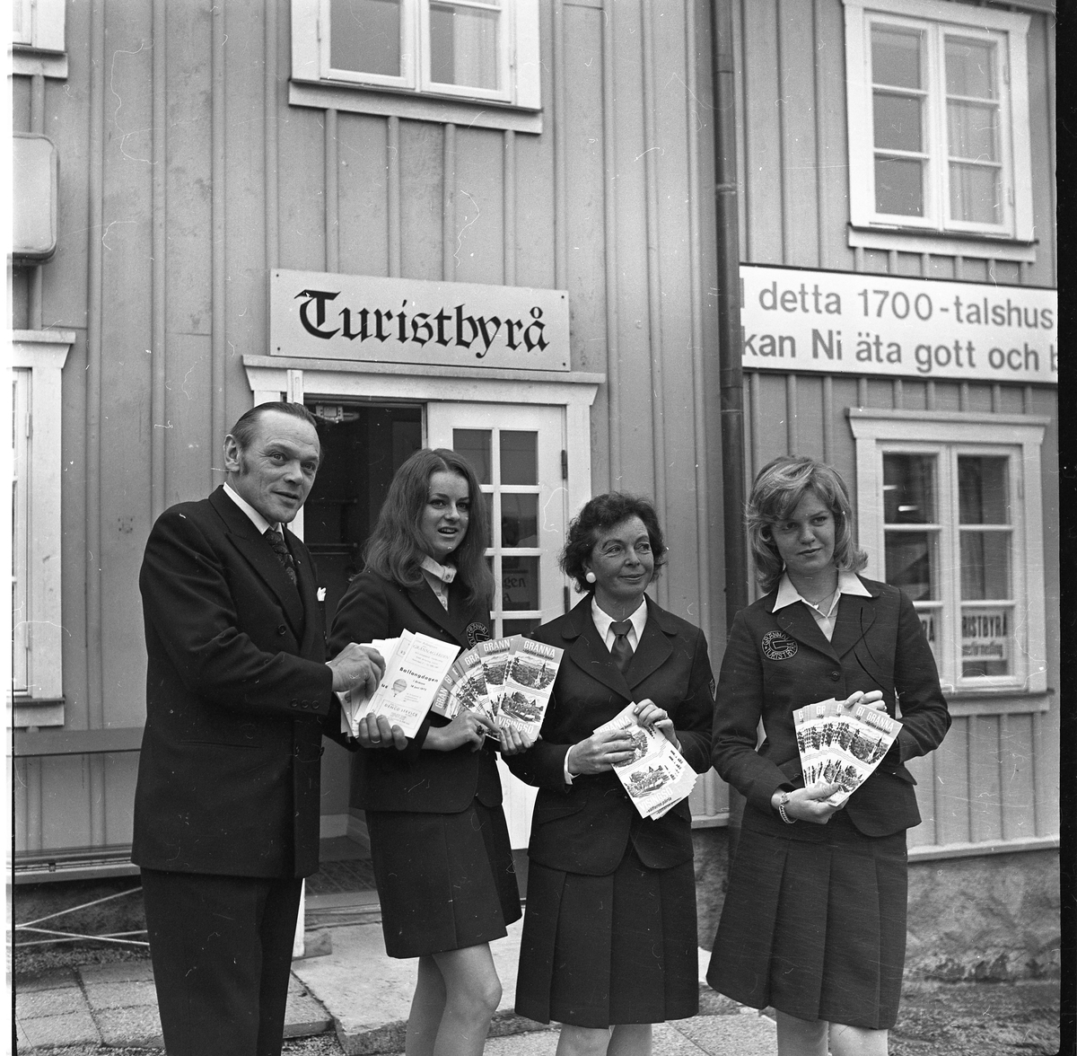 En man och tre kvinnor, i uniform, står utanför en turistbyrå med turistbroschyrer i händerna.