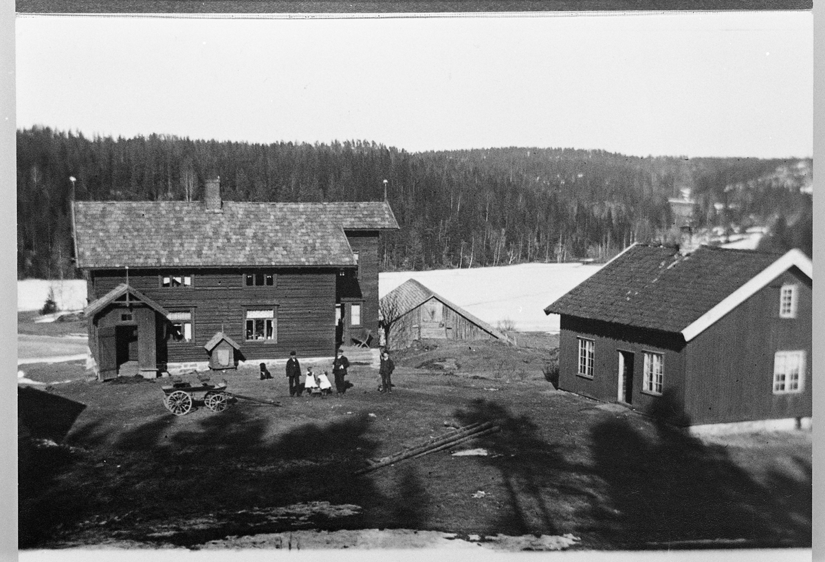 Gårdstunet og bygninger på Hanoa gård i Enebakk april 1911. Noen personer står ute på tunet. Mennene er Johannes, Gustav, og Mathias Skinderviken. Småjentene Alfhild og Lill Anna Skinderviken.