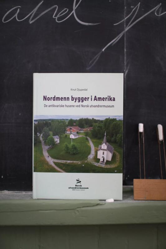 Boka "Nordmenn bygger i Amerika - De antikvariske husene ved Norsk utvandrermuseum", forfatter Knut Djupedal. Boka står foran tavla i skolestua på Norsk utvandrermuseum