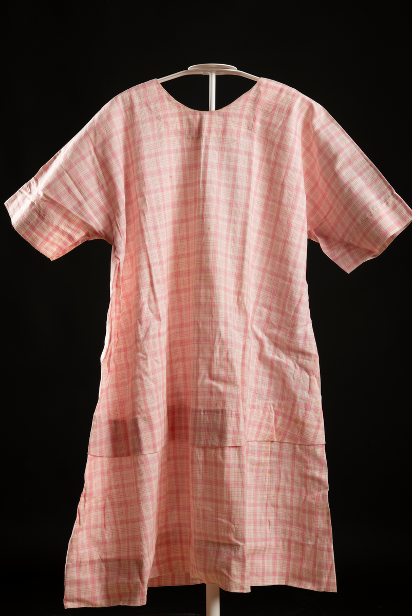 Kortärmad klänning av rosa rutigt tyg. 5 cm brett upplägg i knähöjd.