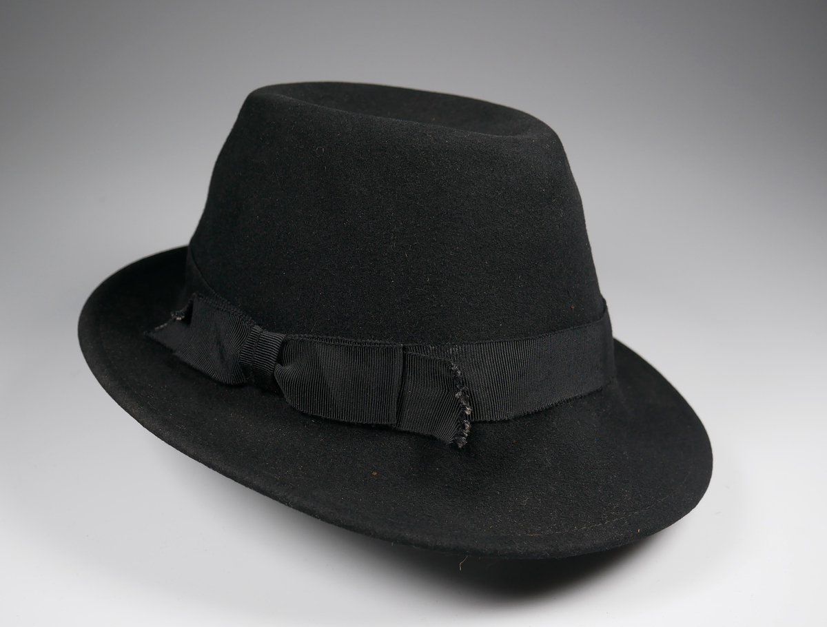Svart damhatt av fedoramodell. Av filt. I hatten finns en etikett från "Ellen Bäckström Tel.673 Alingsås". 
Fodret mycket trasigt.