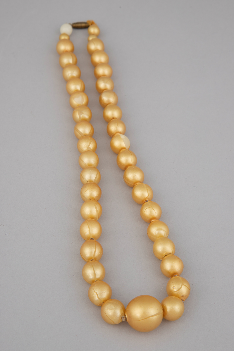 Halskjede bestående av 39 gule perler med små glassperler imellom. Perlene er ordnet med 19 på hver side av en større perle. Av de 19 er 17 omtrent like store, mens de to nærmest låsen er mindre, hvorav den største er nærmest låsen. Enkel gullfarget skrulås.