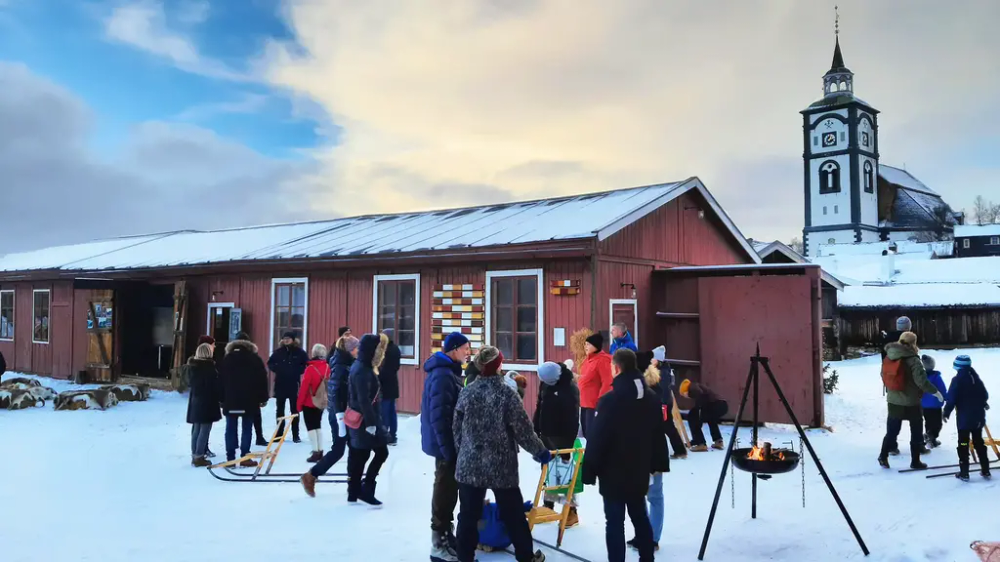 Bildet viser en gruppe mennesker ved ei bålpanne. I bakgrunnen ser vi et rødt bygg og Røros kirke.