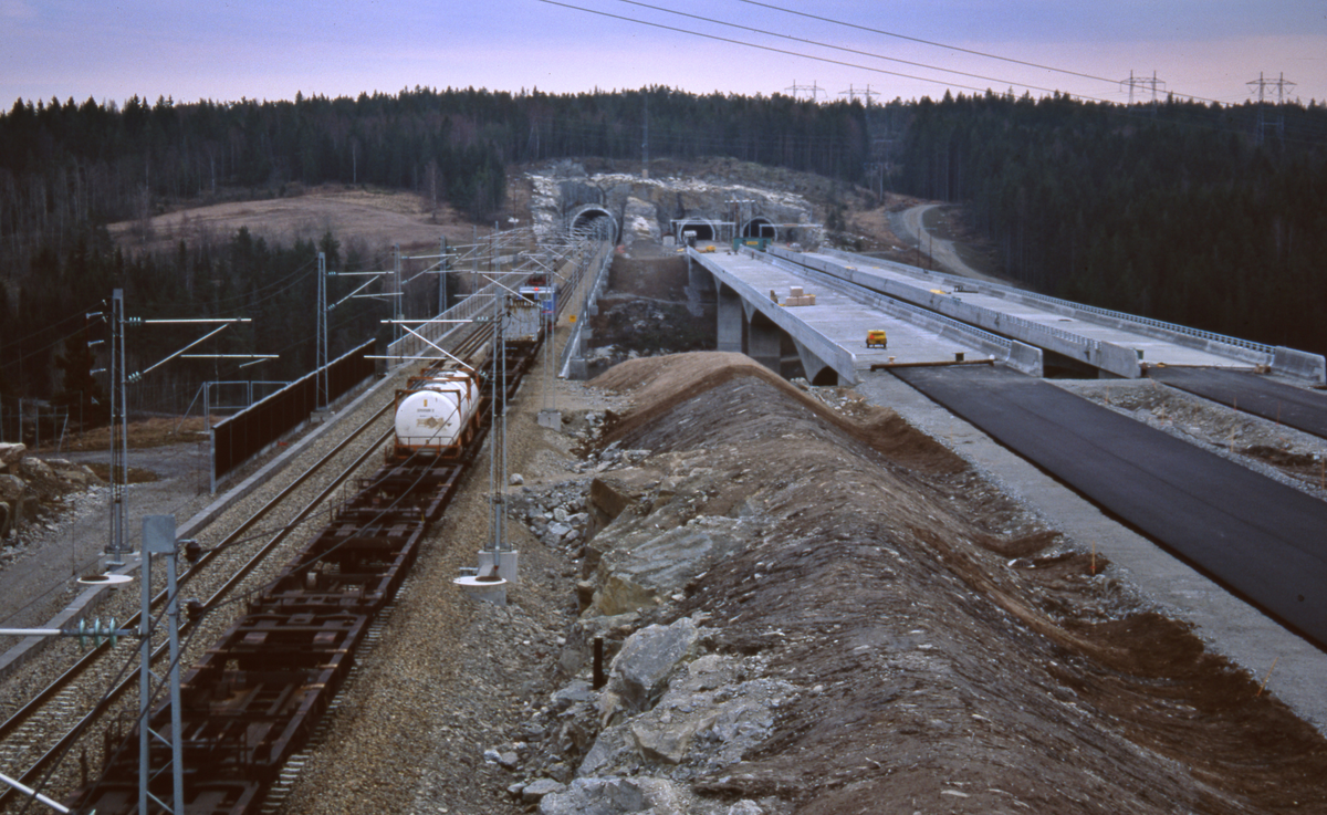 Hølendalen. Nye betongbruer for dobbelt-sporet jernbane (lengst øst/nærmest) og motorvei E6 under oppføring. Godstog på Østfoldbanen. Veien ikke ferdig ennå. Jernbanebru l=416 m, h=50 m, spenn l=128m