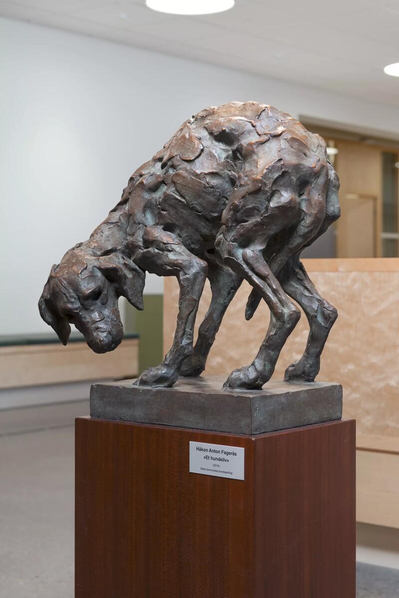 Skulpturen avbilder en hund stående med krummet rygg og halen mellom bena. 
