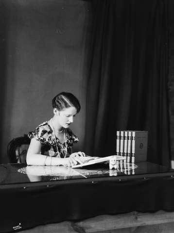 Antatt i studio. Kvinne som leser ved et bord med bøker. Gyldendal norsk forlag A/S.