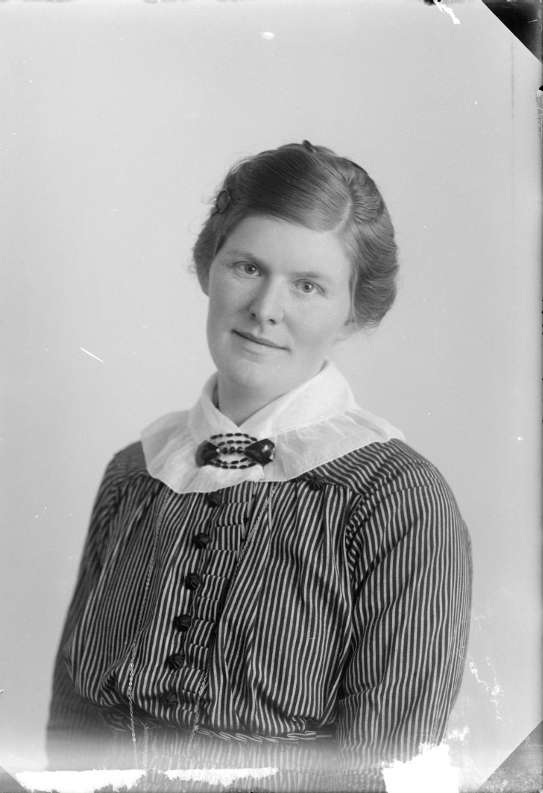 Porträtt av en kvinna i randigt livstycke med svarta klädda knappar, vit spetskrage och brosch.