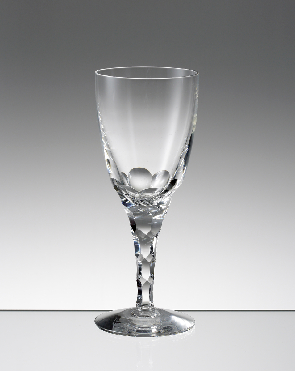 Design: Ingeborg Lundin.
Vitvinsglas. Tulpanformad kupa med fasettslipad nedre del. Konande ben med fasettslipade fjäll.