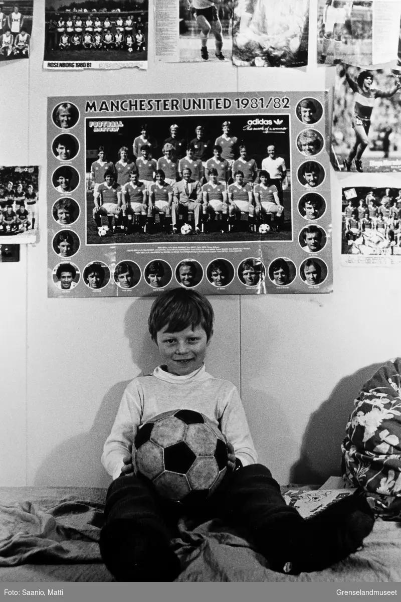 Bilde tatt i Bugøynes på 80-tallet. Vi ser Espen Pedersen på gutterommet, sittende på sengen med en fotball i fanget. På veggen over han henger flere fotballplakater, blant annet spillerne i Manchester United sesongen 81/82.