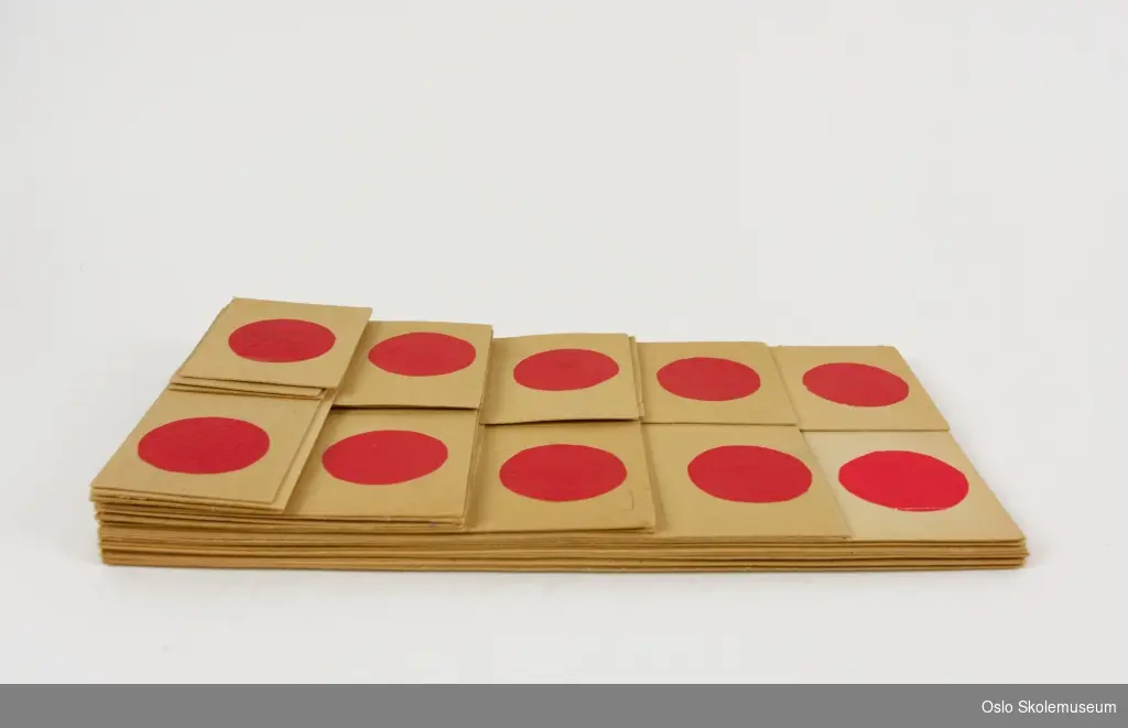 Mattespill i kartong. 27 kort i forskjellige størrelse som representerer tallene 1 til 10 ved hjelp av røde prikker. Størrelsen på kortene avhenger av antall prikker.