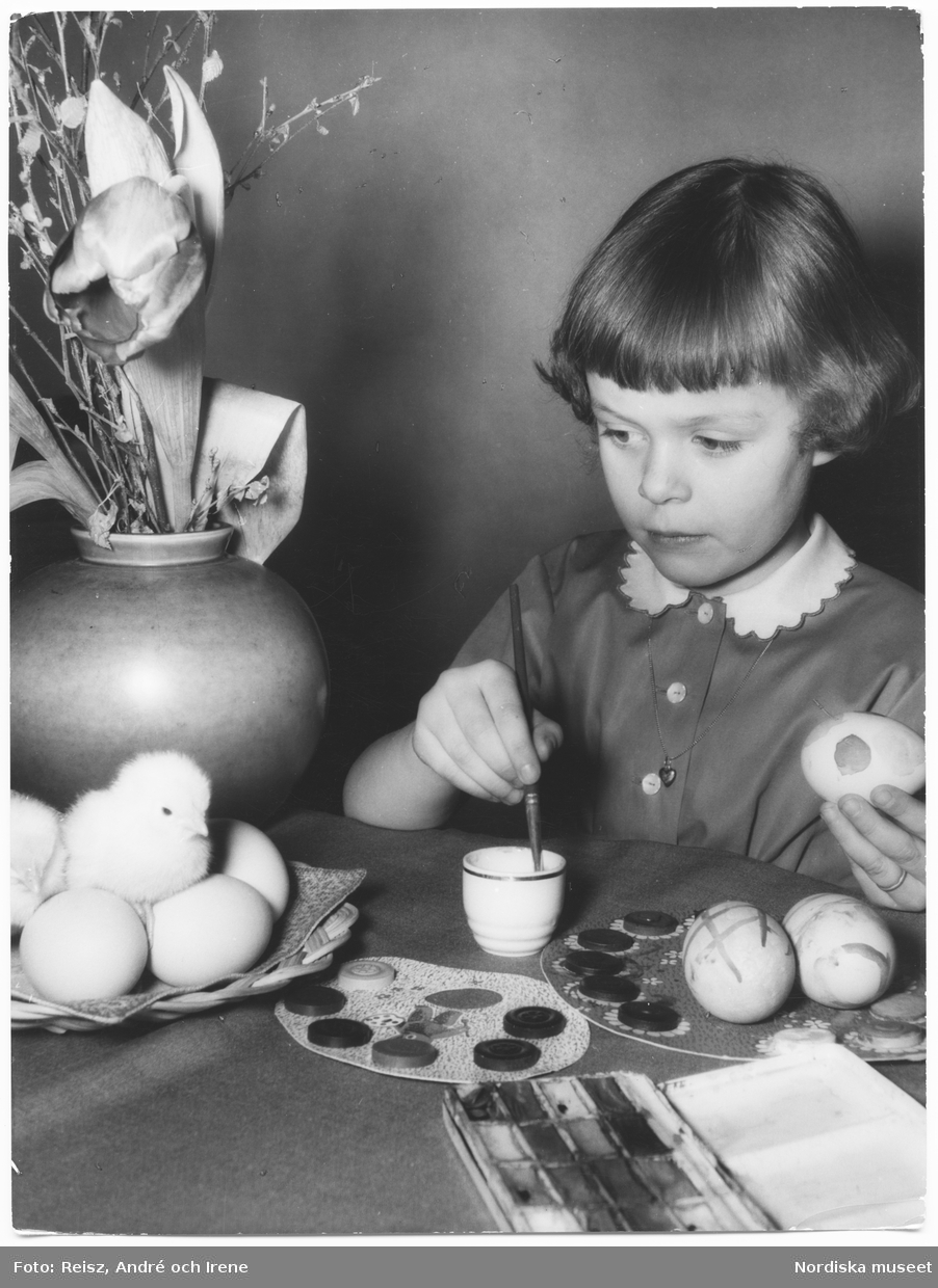En flicka målar ägg och tittar på en kyckling.