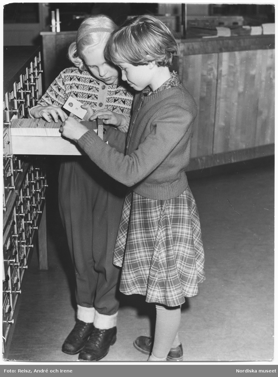Två flickor på Barnbiblioteket vid Gärdet tittar genom bibliotekets kartotek / kortkatalog.