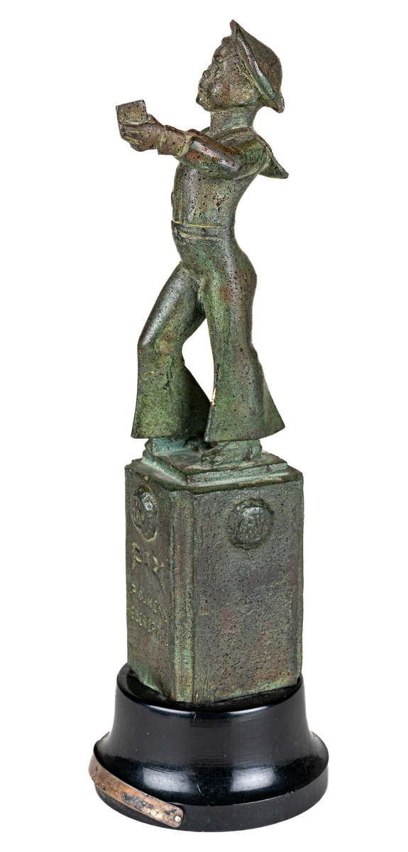 Liten skulptur i brons, med svart träfot, föreställande Pix-pojken. Text i relief på skulpturens bas: Pix pojkens hederspris.