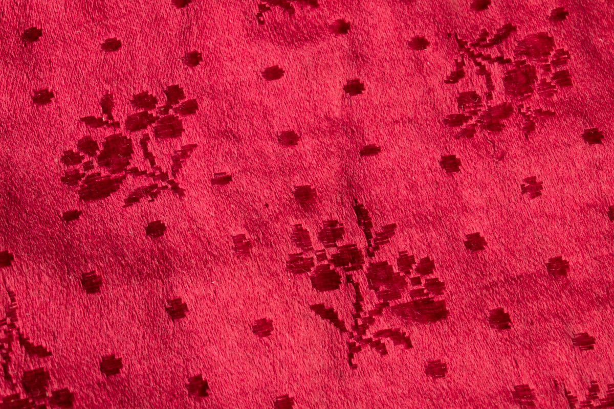 Rektangulær, etui av rød silke. Blomstermønster  vevd inn i silken. Svart innvendig. Grå lommevegger. Kan lukkes med lilla sløyfe bånd som surres rundt flere ganger