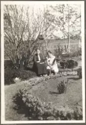 To kvinner sitter i en hage ved blomsterbed