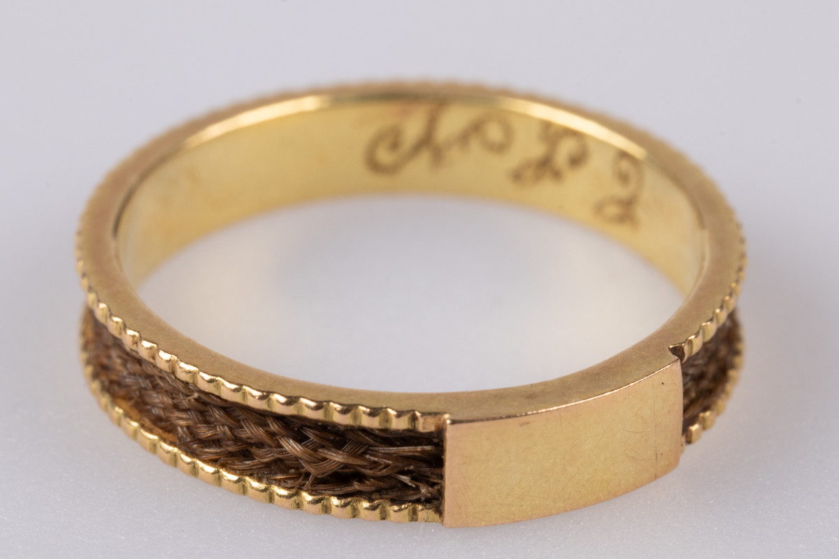 18 karats gullring med flettet hår rundt yttersiden av ringen. På innsiden er der et legeringsstempel og inngravert monogram