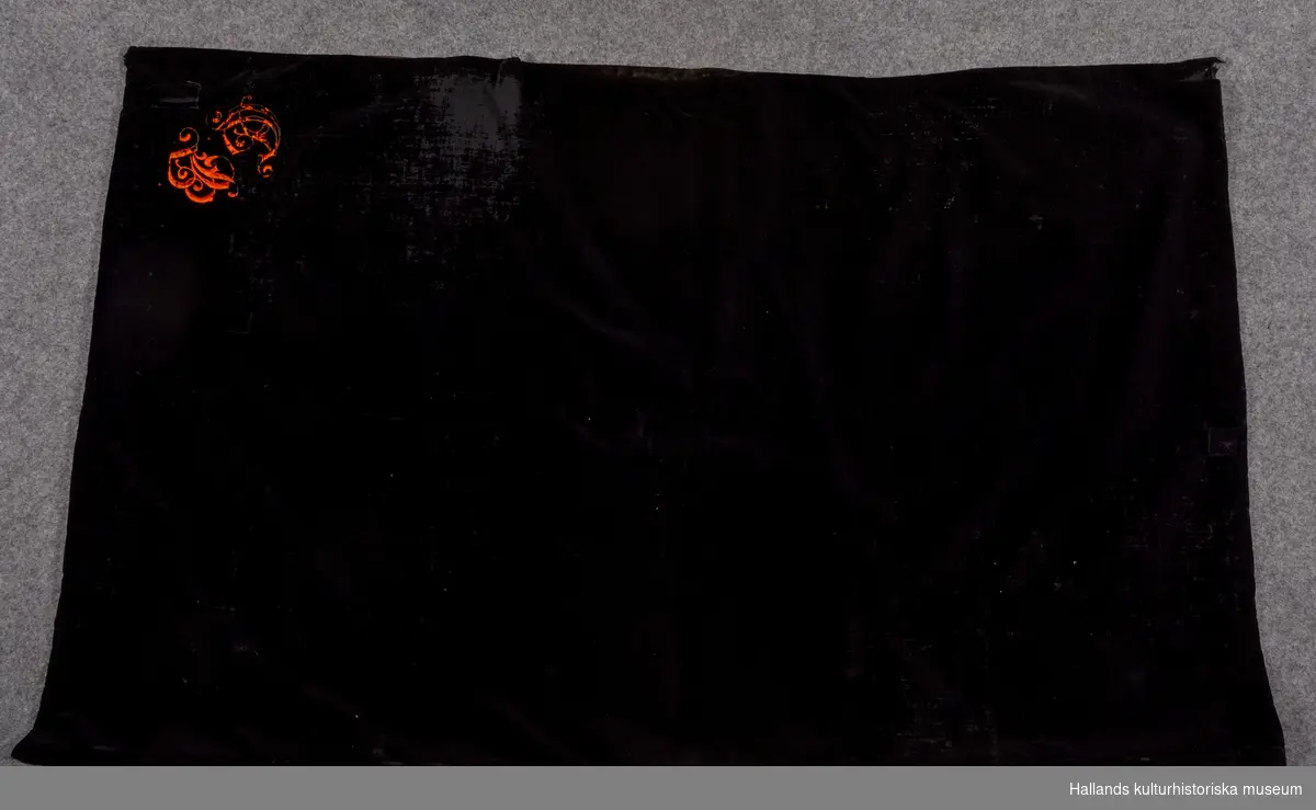 Mörkläggningsskynke av sammet för kamera. Svart, fodrat med svart taft. Monogram i ena hörnet "G B", sytt i plattsöm med orange silke. Längd: 140 cm. Bredd: 88 cm.