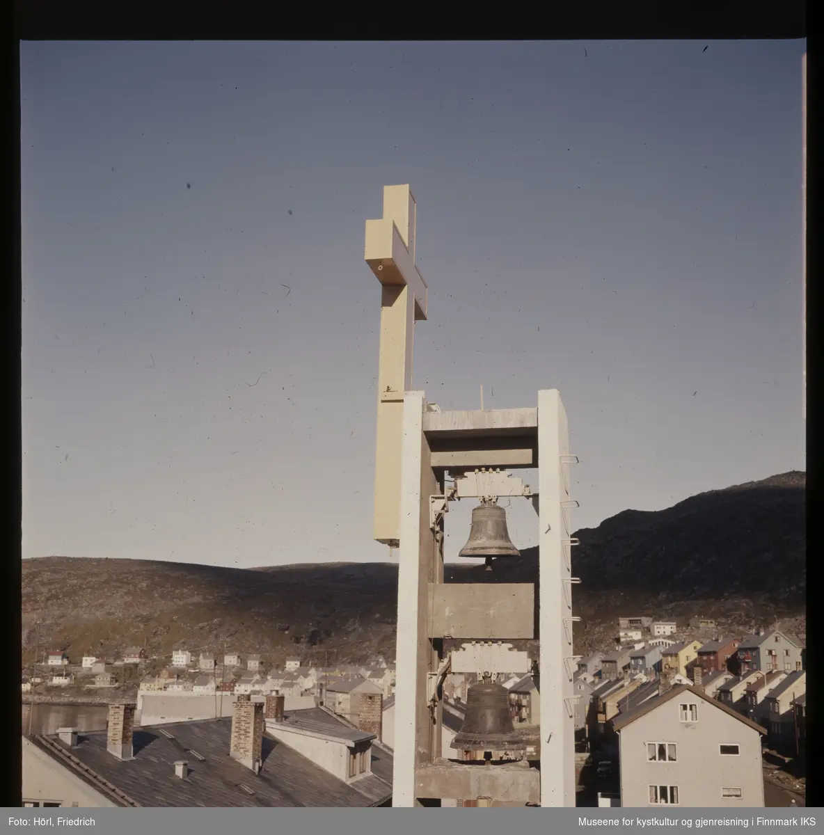Det slanke klokketårnet til Den katolske kirke St. Mikael i Hammerfest har reist seg over gjenreisningsbyen. Klokkene fra den gamle Hammerfest kirken er hengt opp igjen. Gjennom heldige omstendighetene kunne de reddes for smelteovnene. Tårnet er pyntet med et fire meter høyt, lyssatt kors. I bakgrunnen ser man Mollafjellet.