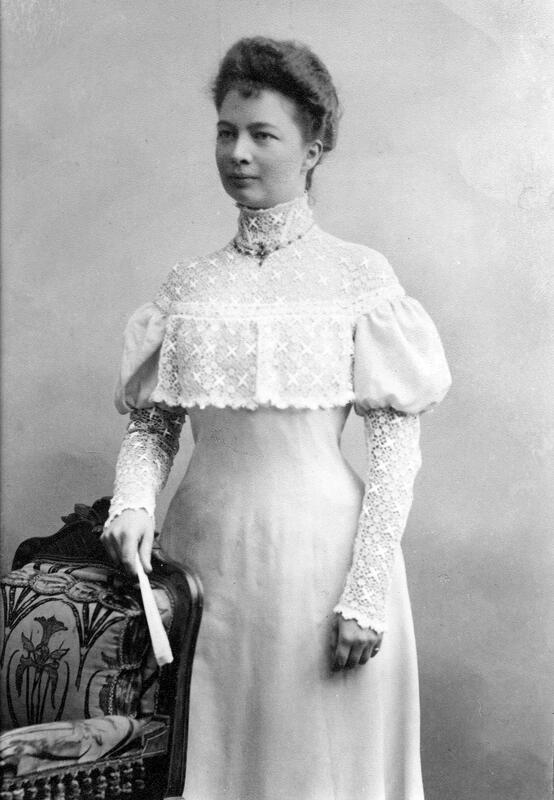 Svart/hvitt foto tatt hos fotograf fra rundt år 1900. Viser ung kvinne i tidstypisk lys lang kjole, med oppsatt mørkt hår. Kvinnen på bildet er arkitekten Hjørdis Grøntoft.