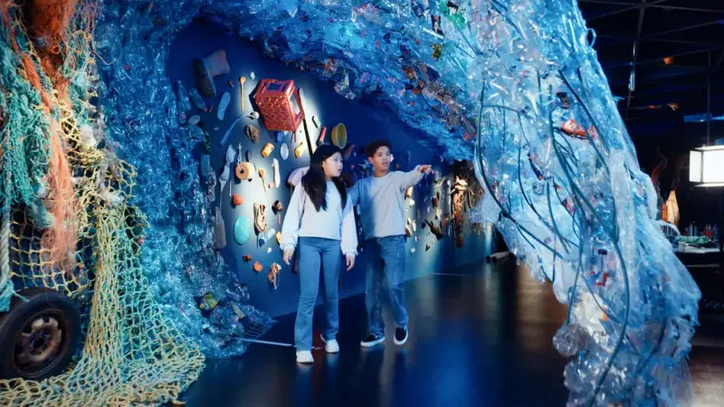 Barn som går under en plastikbølge i utstillingsrom fra Oppdag havet på Norsk Maritimt Museum.