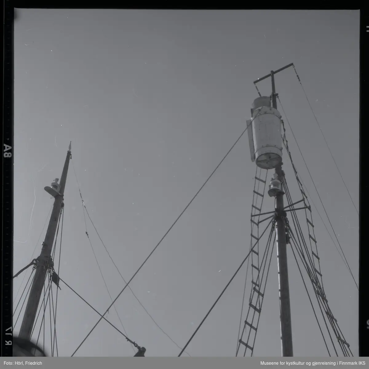 Bildet viser to master til en fangstbåt, mest sannsynlig fotografert fra kaia og skrå oppover. Godt synlig er den karakteristiske utsiktstønna i masten til høyre.
