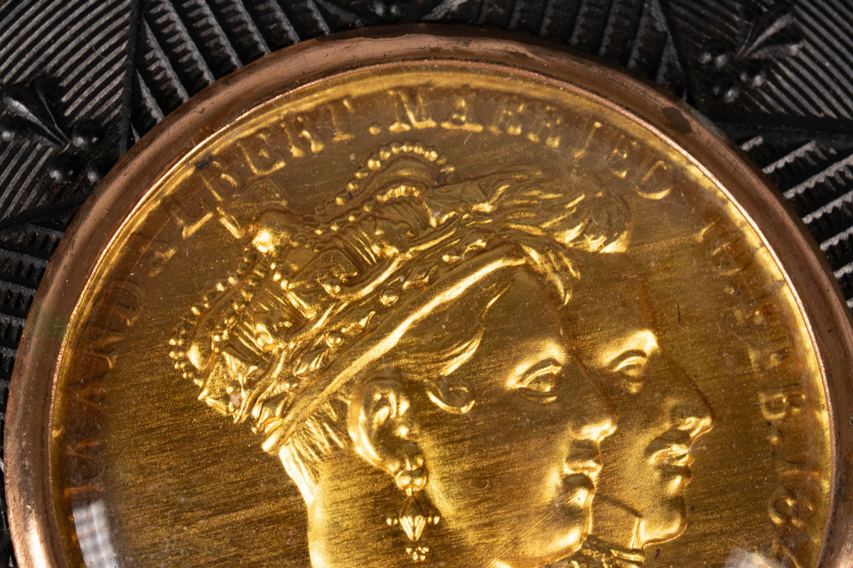 Relieff av profilen til dronning Victoria i front og prins Albert bak henne. Dronningen har krone på hodet. Prinsen har gallauniform.