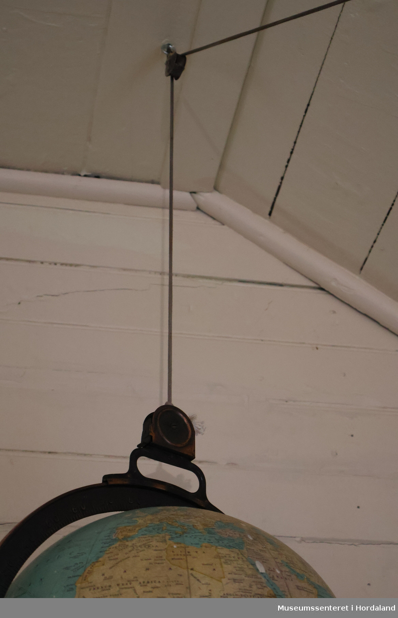 Globus med en ring av metall rundt som har grademål. Globusen henger fra taket i en snor som er trukket gjennom trinse i tak og på vegg, med et kulerundt lodd i enden ved gulvet.