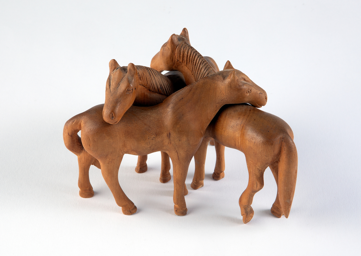 Tre stycken snidade hästar av trä tänkta att stå i grupp med halsarna vilande på varandras manke.
