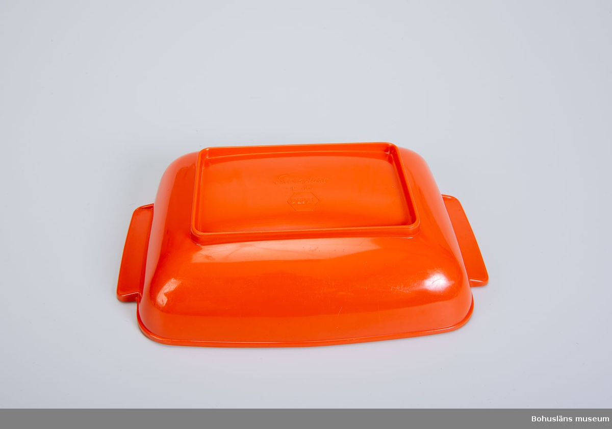 Rektangulärt serveringsfat eller uppläggningsfat med rundade kanter med dekorerade handtag i orange melaminplast.