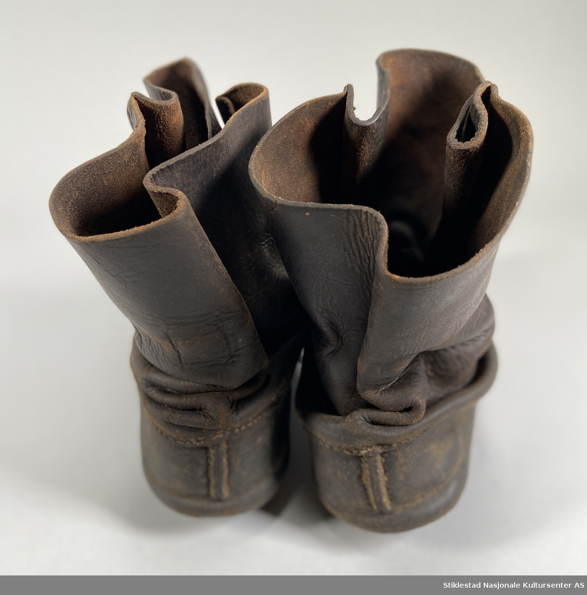 Et par skinnsko kalt "lauparsko?" med skinnreimer (snøring) for å feste rundt skoene. Snøringen er sydd fast mellom to sømmer i skaftet. Sålelær er sydd sammen med overlæret. Skoene ser ut til å ha hatt såler, men disse er fjernet (tydelige spor etter fjerning). Uforet sko. Størrelse 45.