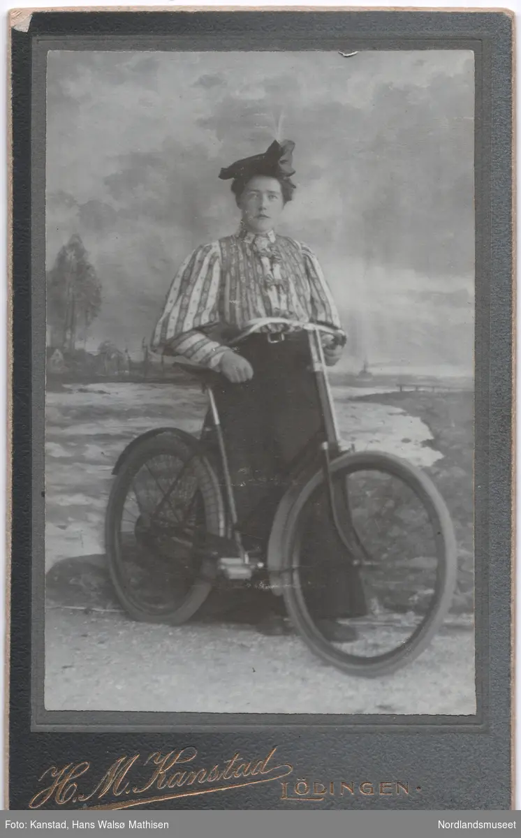 Portrett av en ung kvinne, Lulla Fremmerlid, med sykkel foran malt lerret, utendørs.