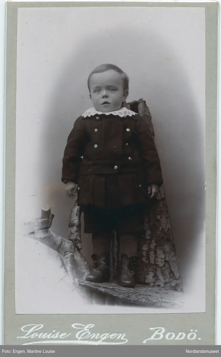 Portrett av en liten gutt i korte bukser, lærstøvler, dressjakke og hvit krage.