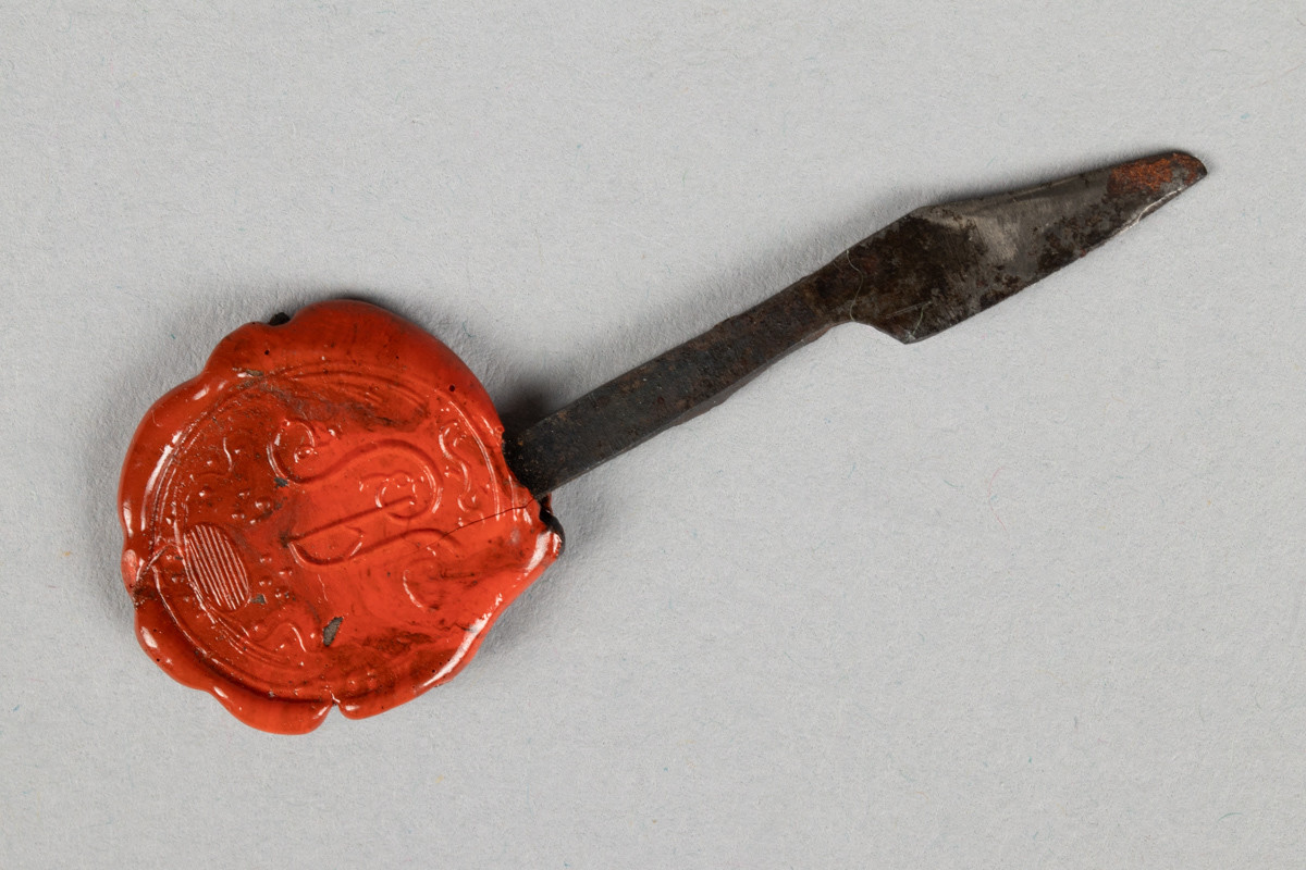 Pennekniv i metall med et segl i rød lakk festet på skaftet