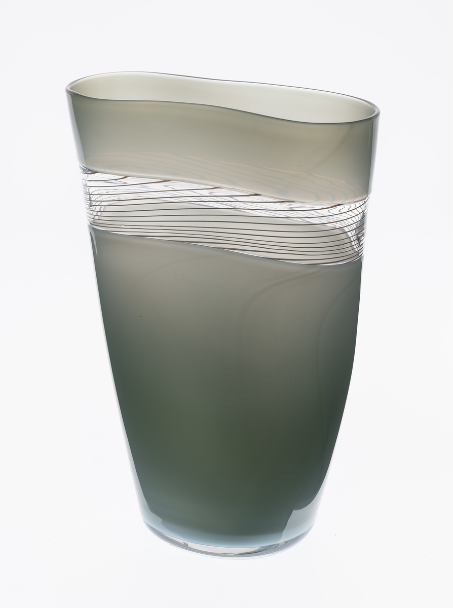 Konisk høyreist vase i polykromt glass med innsvunget midtparti og åttekantformet munningsrand. Vasens øvre og nedre del er utført i grågrønt halvgjennomskinnelig glass, mens det smale midtfeltet er utført i klart glass med hvite emaljetråder.
