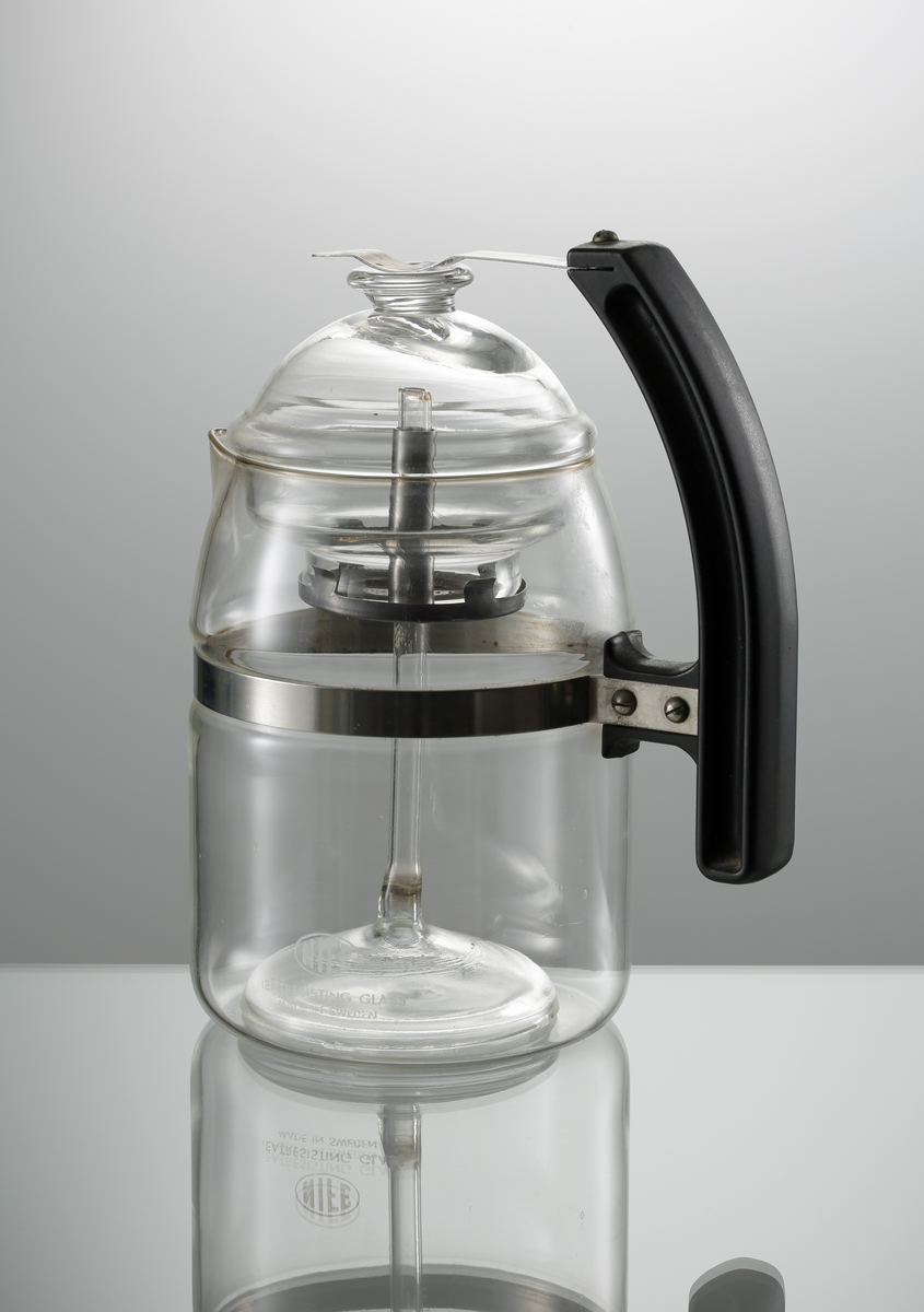 Kaffebryggare med lock, tillverkad åt NIFE. Artikelnummer KB 60 för bryggning av 1.5 liter kaffe (KB 40 för bryggning av 1 liter). Cylindrisk med formad pip. Handtag i bakelit, som sitter fäst i en rostfri ring runt livet. Överst på handtaget en rostfri bygel, som håller ner locket. Under locket en monterad sil, i vilken ett glasrör löper genom.
