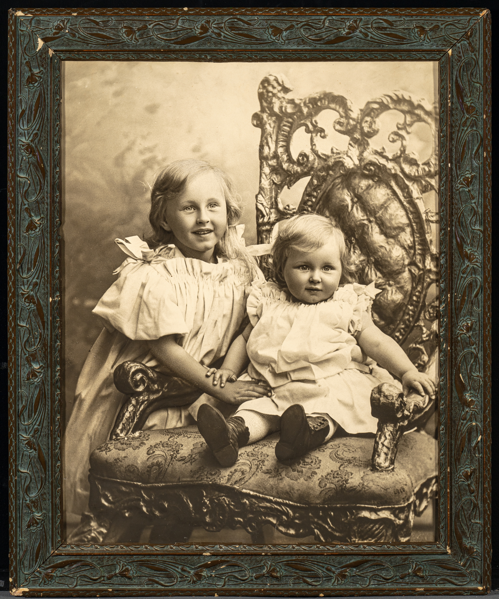 Et sort-hvitt fotografi i glass og ramme. Det er et stort barneportrett av to små jenter (søstrene Johanne Marie Knoff Worsøe og Bergljot Knoff Gilberg). Til høyre på bildet er det en stol med stoppet sete og rygg samt rikt dekorert med utskjæringer i treverket. I stolen sitter den minste jenten i hvit kjole, mørke snøresko og sløyfe i håret. Til venstre står en større jente og holder armen på lillesøsteren. Hun har hvit kjole med korte puffermer og fletter med sløyfer. Rammen er av tre og malt i en mørk brun farge. På rammen er det utskjæringer. Det er en blomsterbord i jugendstil. Fotograf er Gustav Borgen som srbeidet i Christiania/Oslo i perioden 1891-1922. På baksiden av bildet var det stempel fra fotografen, se "Påført tekst/merker"(ble skåret ut av original bakplate og ligger ved bildet).