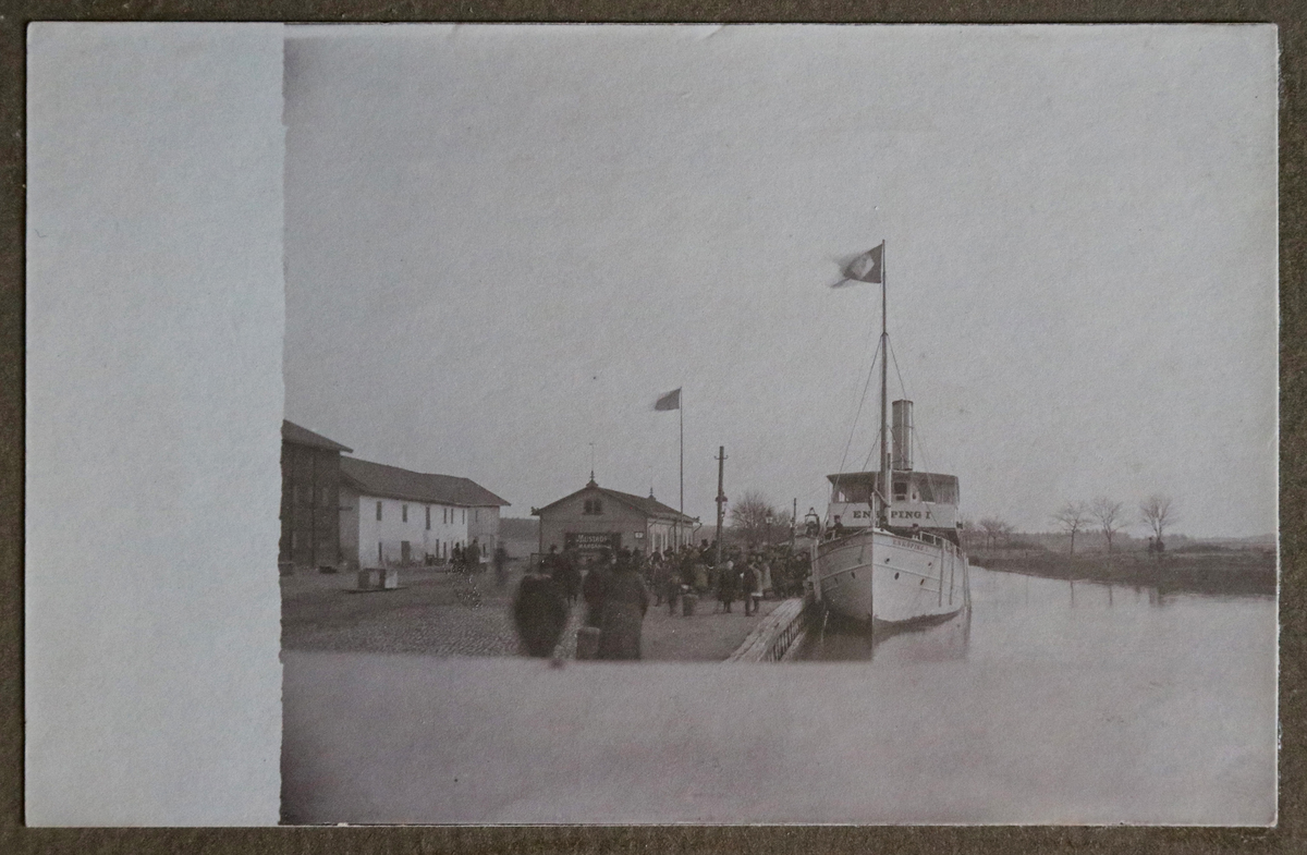 Ett vykort inklistrat i vykortsalbum nr. EM06774_d. Vykortet har motiv från Enköpings hamn. Till vänster i bild skymtar du hamnmagasinen och ångbåten mitt i bild är "Enköping I".