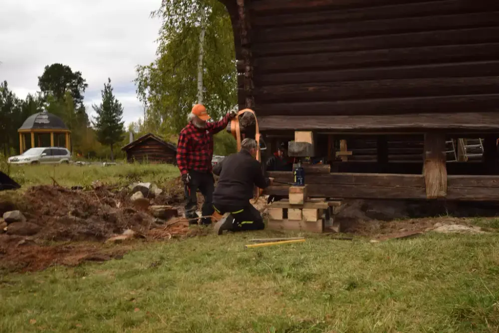 Utsnitt av to menn som arbeider med bygningsvern av et stabbur, de arbeider med å stabilisere bygget