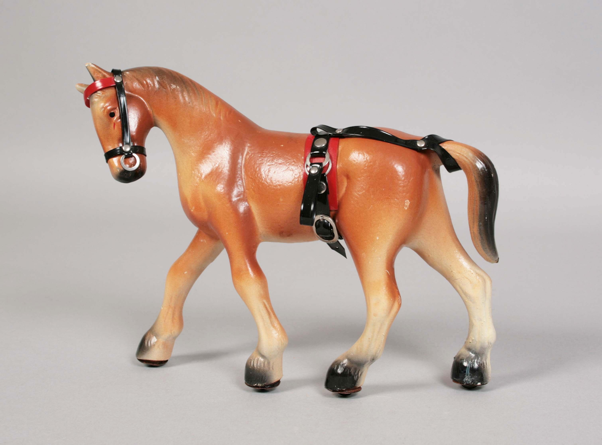Brun häst på 4 hjul av metall. Seldon av röd och svart plast med metallbeslag.