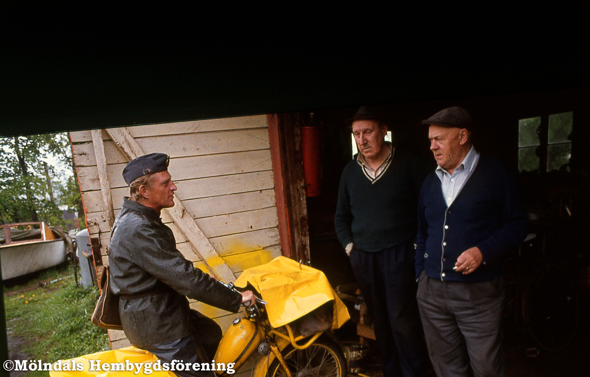 Lantbrevbärare Åke Mattsson lämnar post till Holger Larsson vid dennes smedja på Taljegården i Mölndal, år 1976. Till höger ses även Lennart "Brottar-Lennart" Erikssons farbror Ivar Eriksson, fiskhandlare på Kikås.