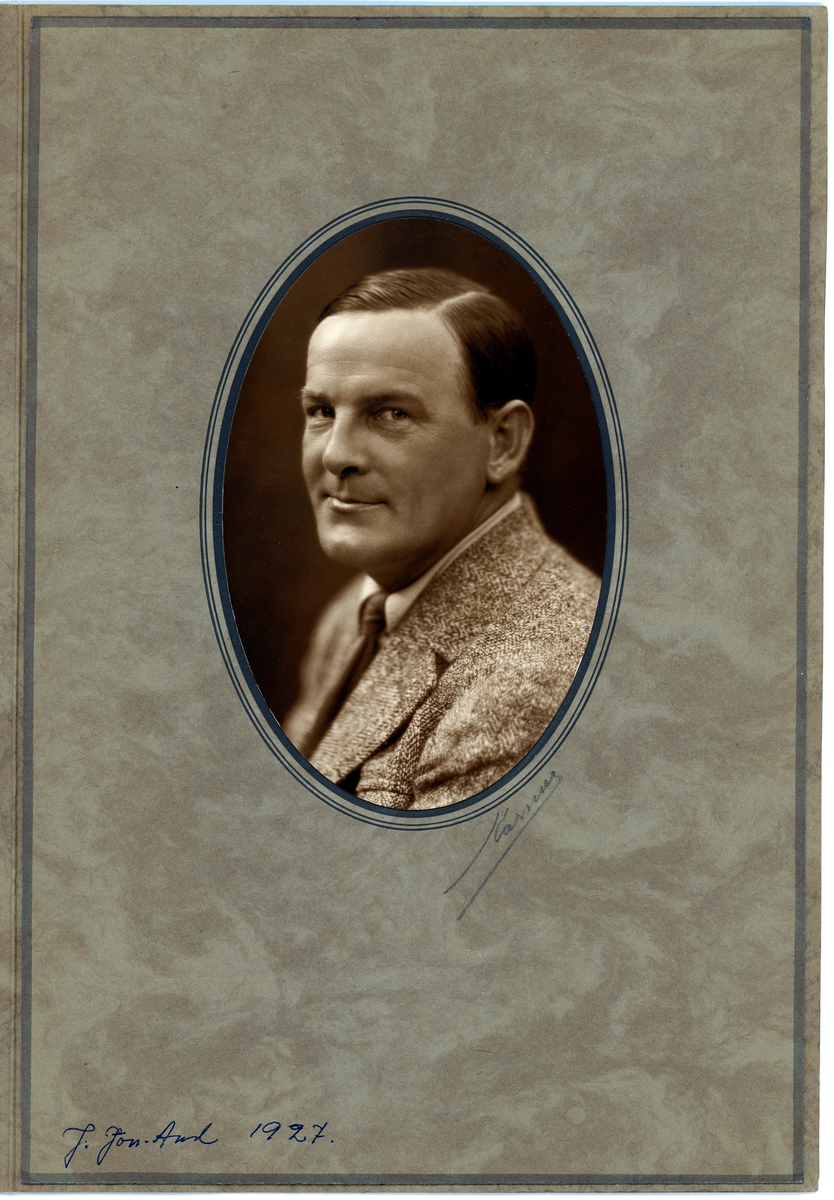 Porträtt av John Jon-And taget 1927.
John iklädd kostym och med välkammat hår.
Porträttet monterat i pappersmapp i formen av medaljong.