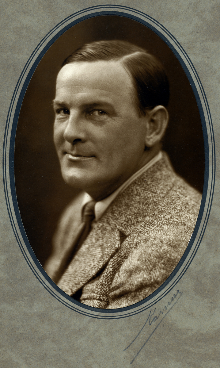 Porträtt av John Jon-And taget 1927.
John iklädd kostym och med välkammat hår.
Porträttet monterat i pappersmapp i formen av medaljong.