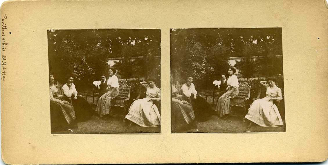 Fyra kvinnor och en man sitter avslappnade i en trädgård.
Stereobild.